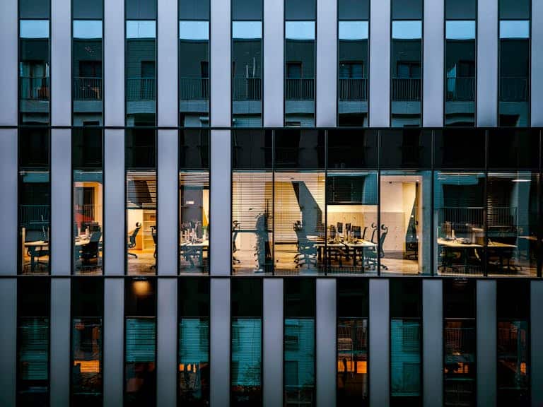 Illuminated office inside a modern glass building exterior, showcasing architecture and workspace design.