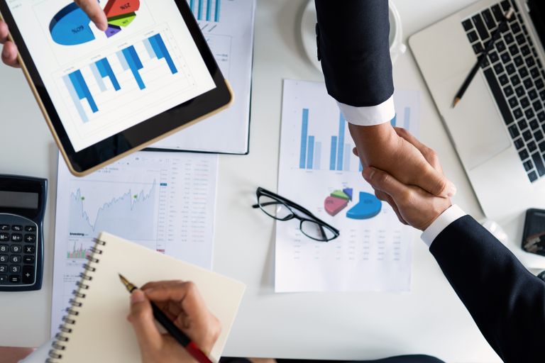The MAR Legal Blog 3 Business professionals handshake over graphs and charts in a corporate setting, symbolizing successful negotiation and agreement.